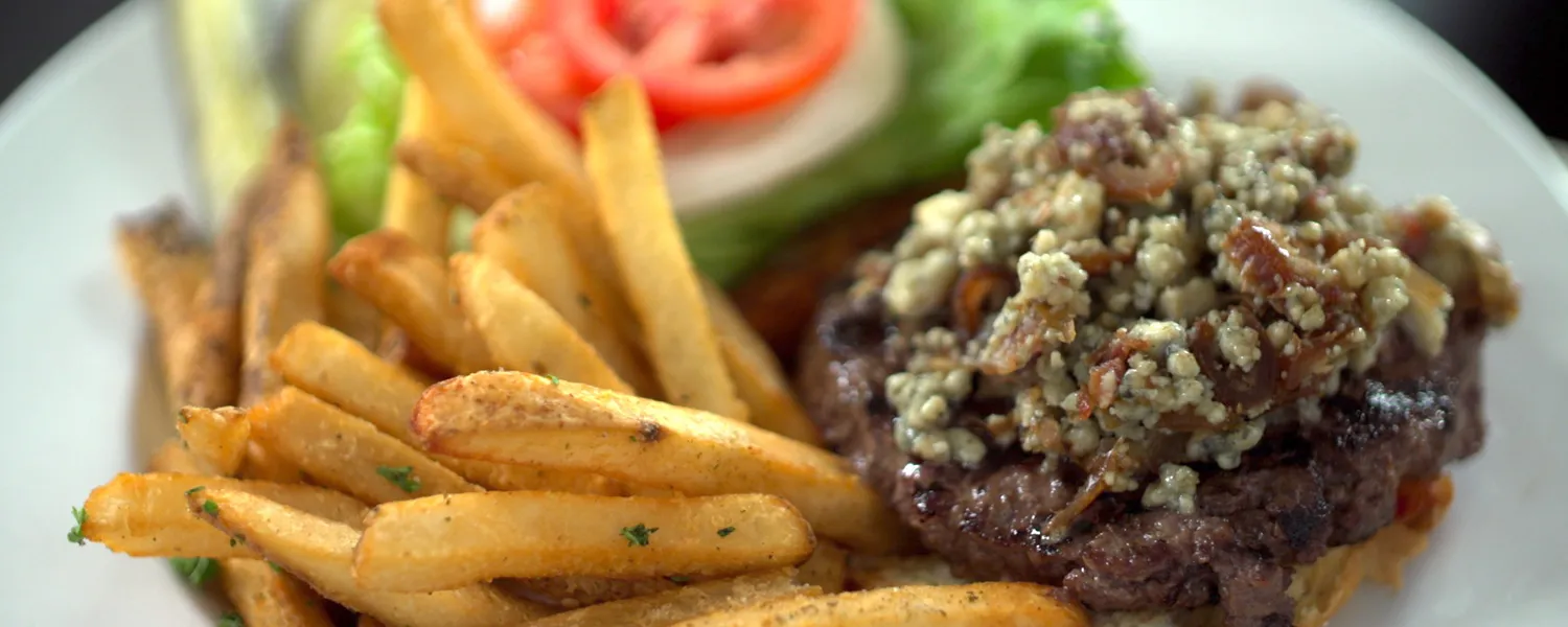 Burger topped with chopped dates and blue cheese, served with seasoned fries