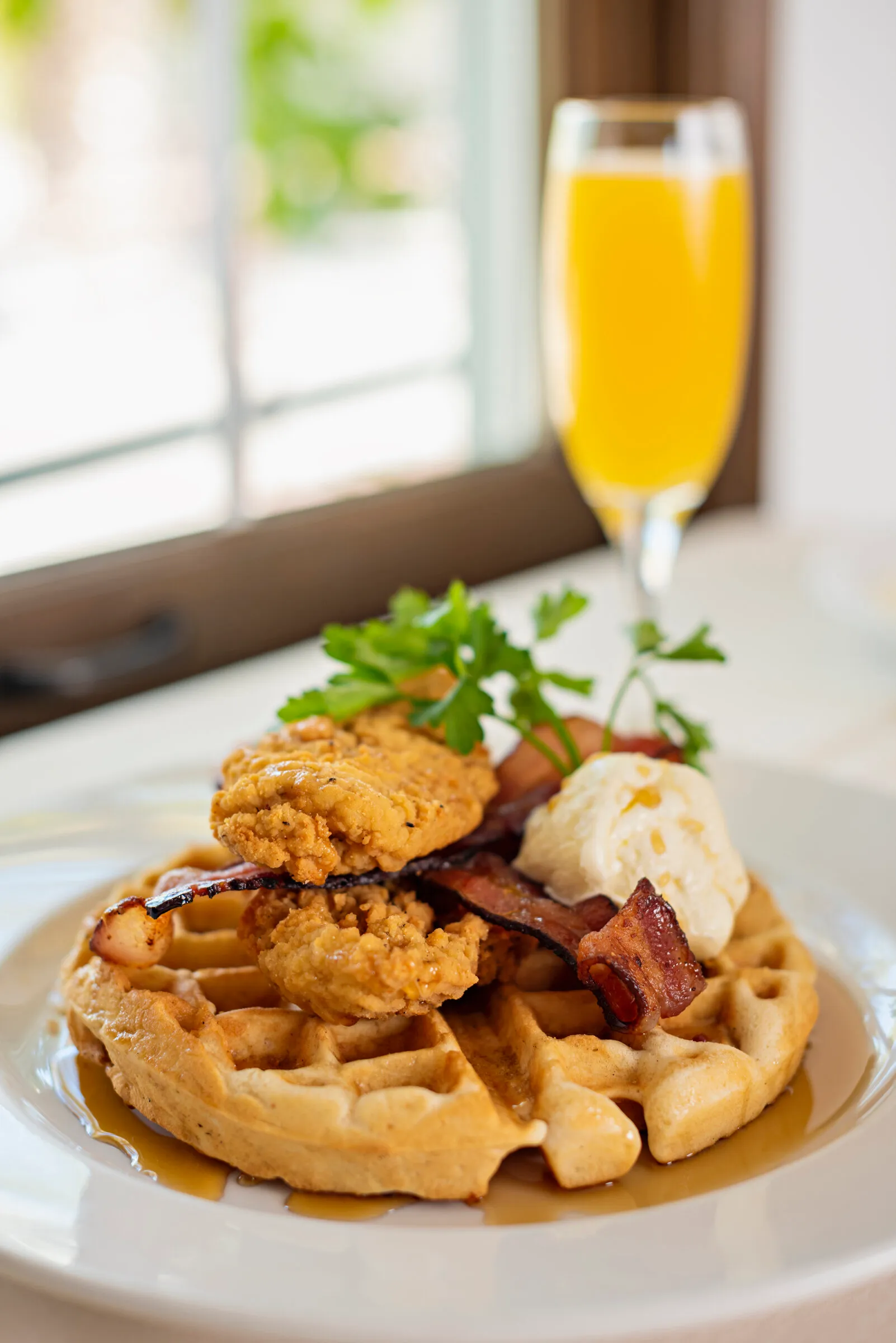 Chicken and waffles topped with bacon and whipped butter, served with a mimosa