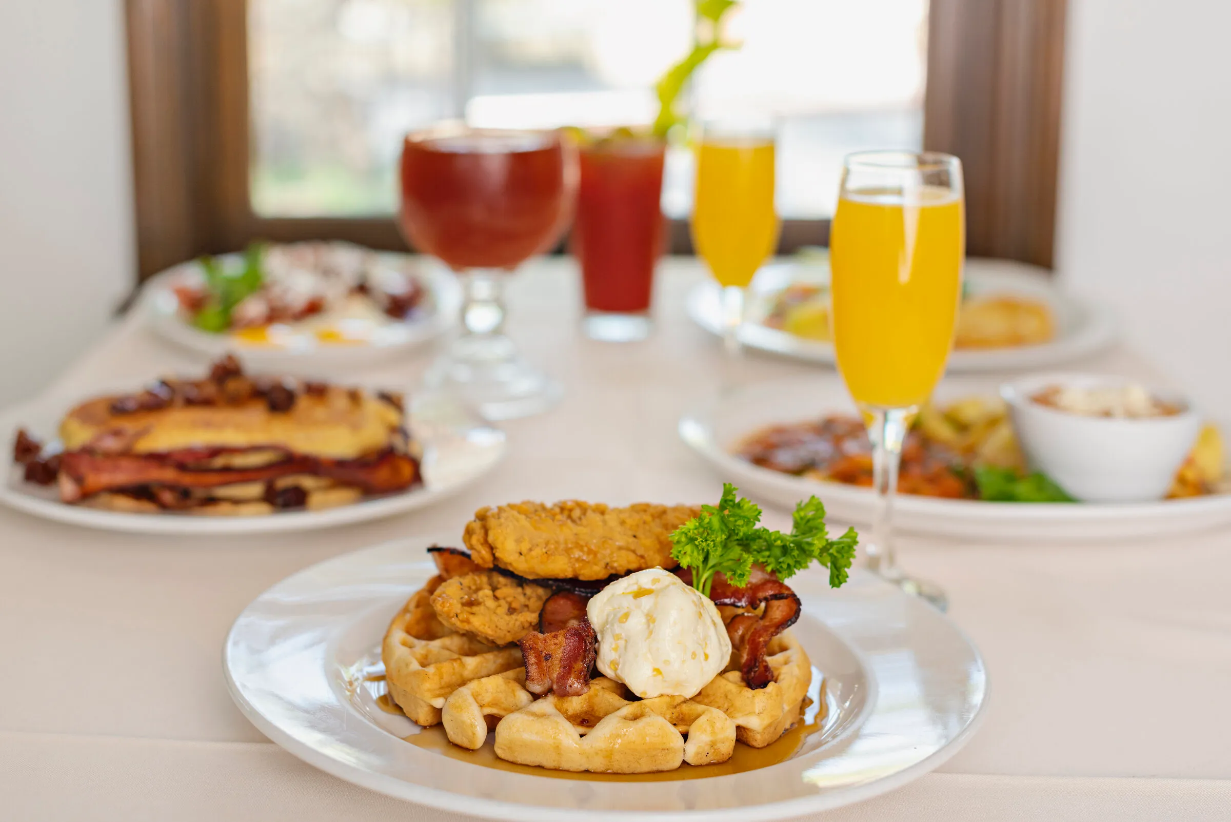 Brunch table with chicken and waffles, pancakes, mimosas, and Bloody Marys