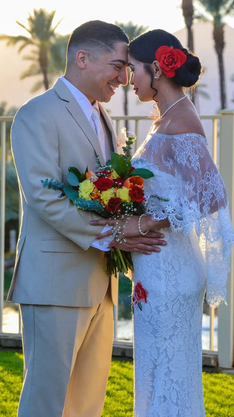 Bride and groom touching foreheads, holding a bouquet of red and yellow flowers