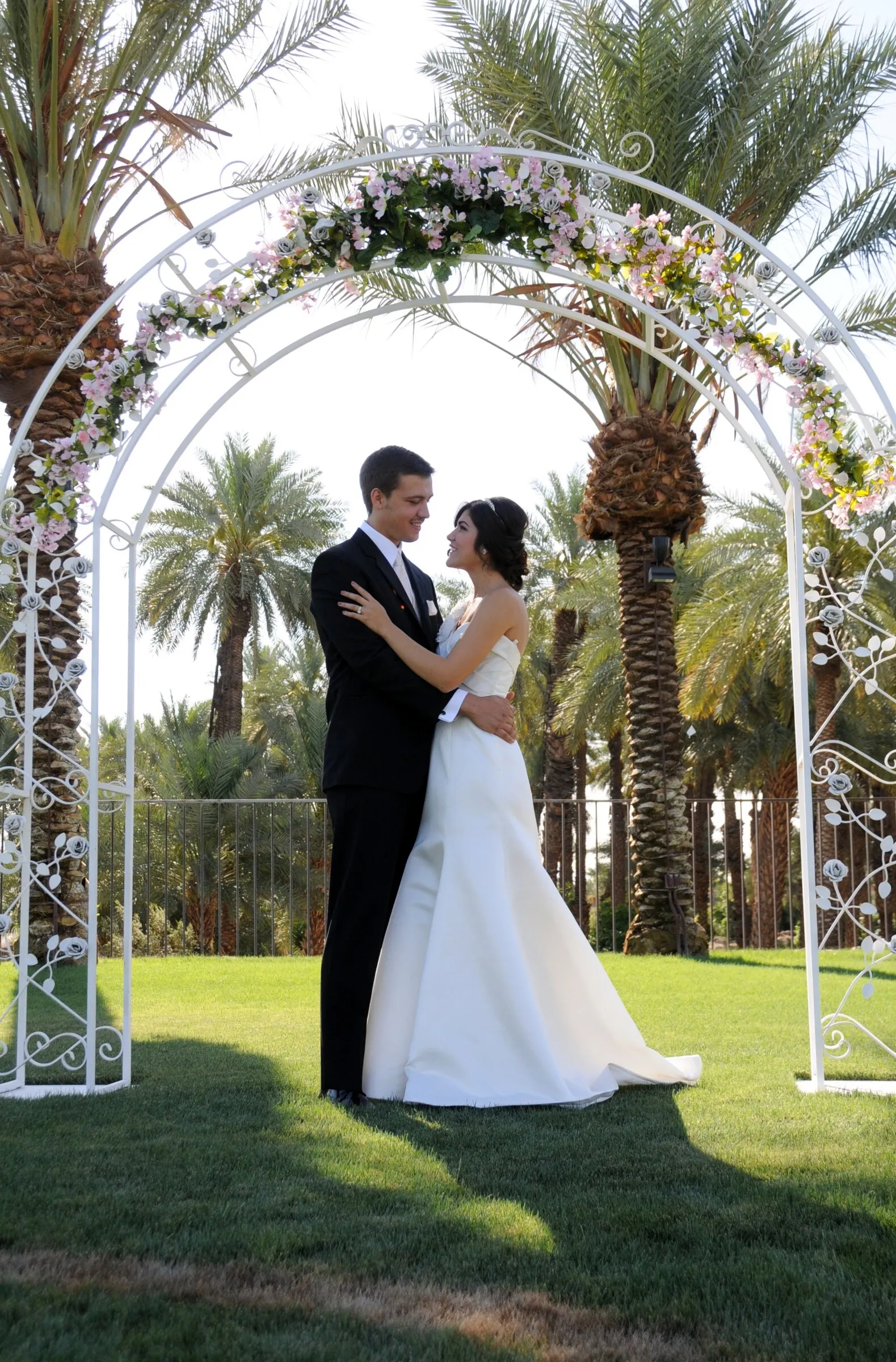 Bride and groom under a white floral wedding arch in the palm garden